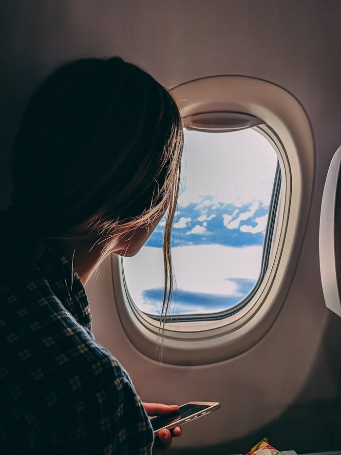 Mastering the First Impression: Your intriguing post title goes here A woman looks out an airplane window, capturing a serene view of clouds and sky during a flight.
